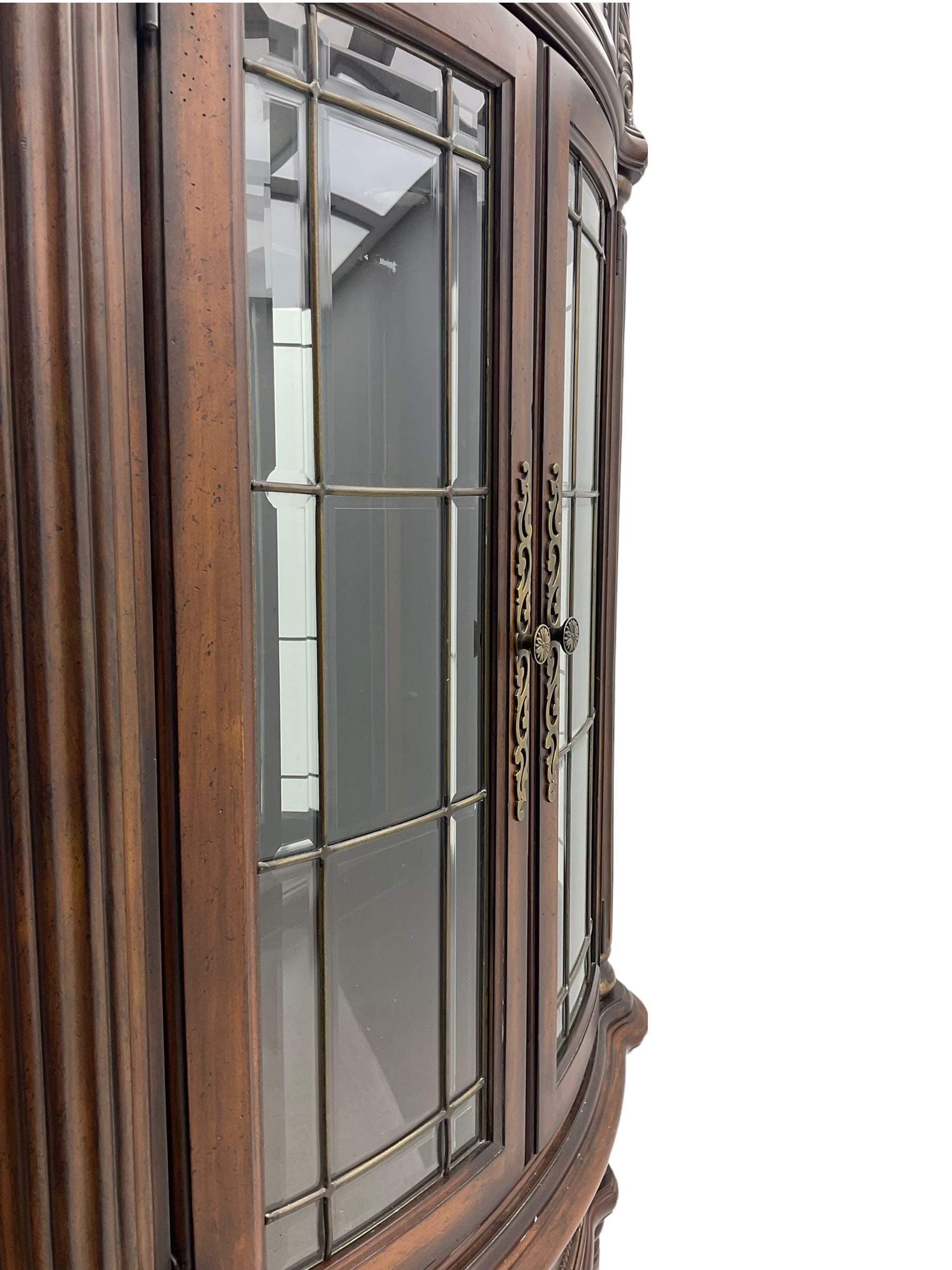  Kevin Charles American walnut demi lune display cabinet with illuminated interior, projecting cornice, two bevel edge glazed doors enclosing two adjustable shelves above single drawer and four cupboard doors with wine rack, carved scrolling supports