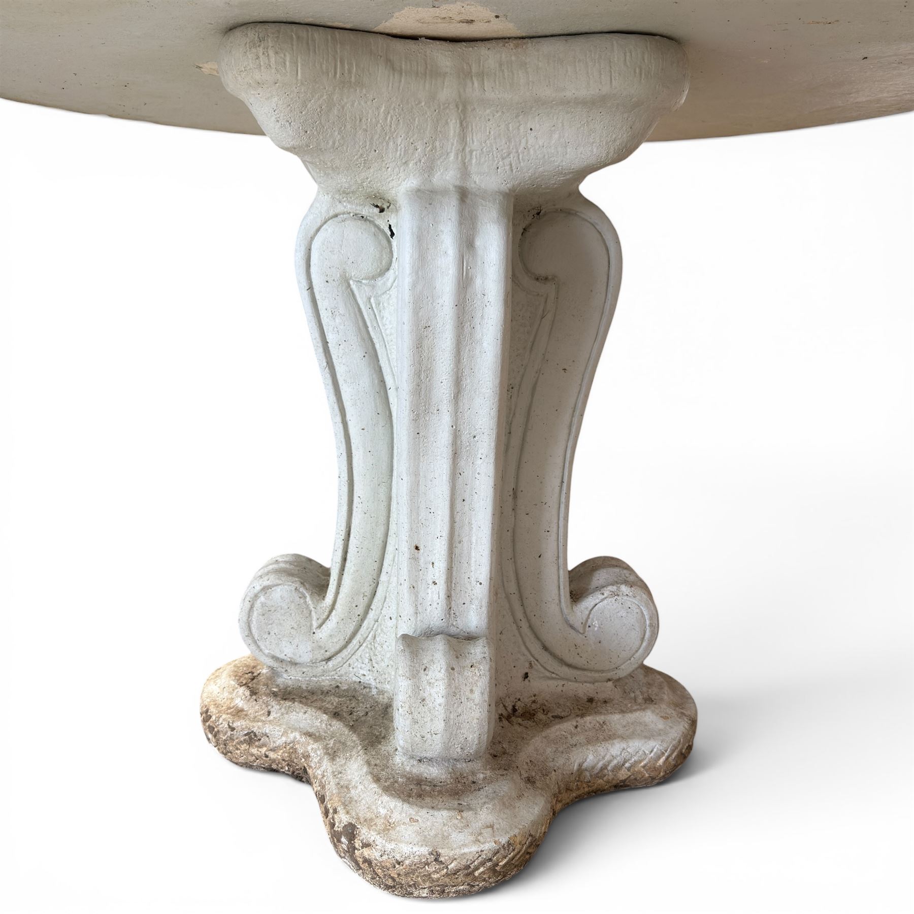 Weathered cast stone garden table, circular top etched with central floral medallion, the edge with repeating chevron motifs, raised on a quadriform S-scroll pedestal with stepped and chevron carved base