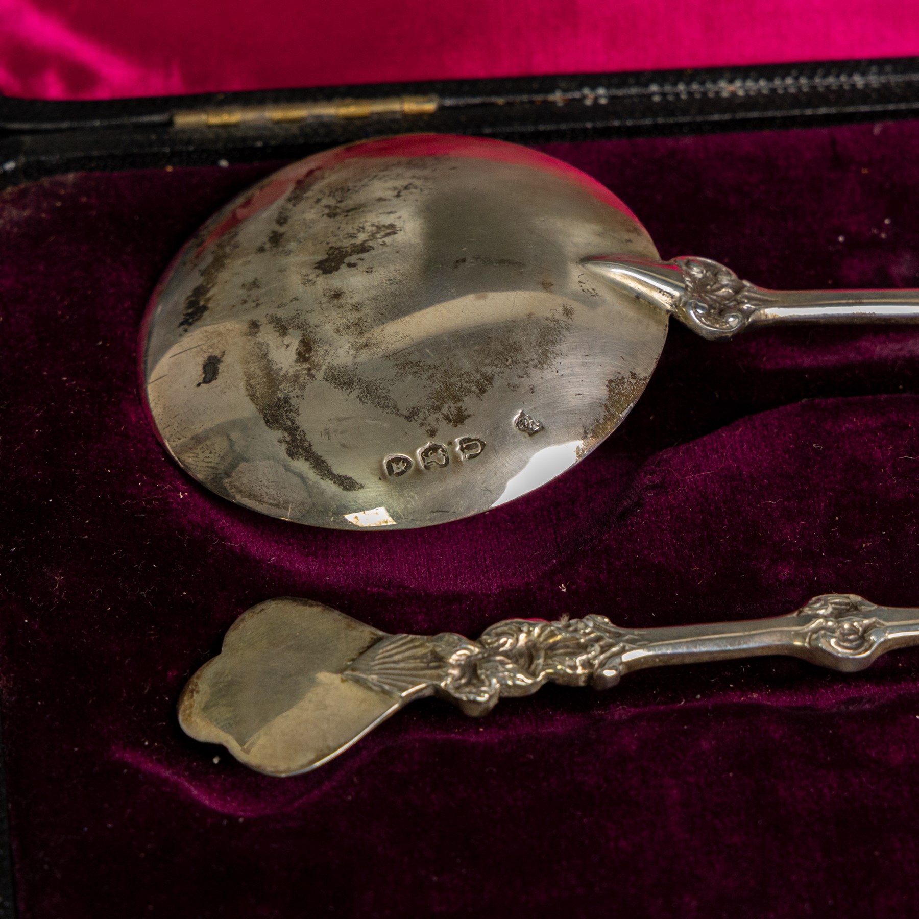 Pair of late Victorian silver serving spoons, each with circular gilt bowls and embossed putti decoration, hallmarked William Hutton & Sons Ltd, London 1895, contained within a tooled leather box with burgundy velvet and silk interior