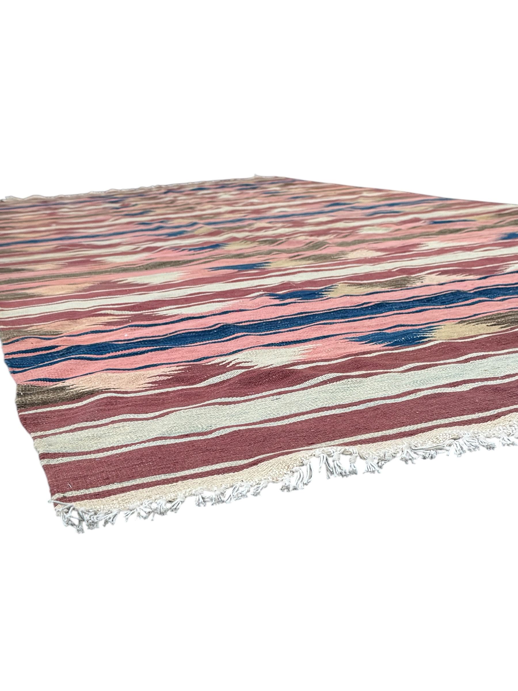 Kilim muted pink ground runner, decorated with rows of horizontal bands in muted tones, alternating with geometric triangular patterns along each band, fringed ends