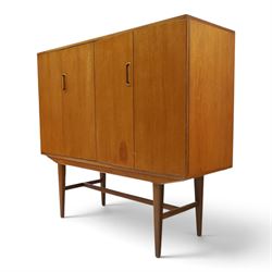 Alfred Cox - mid-20th century teak cabinet, rectangular top over two bifold doors with inset handles, opening to reveal three central graduating drawers surrounded by assorted shelves, raised on tapering supports united by H-stretcher, stamped to inside of drawer