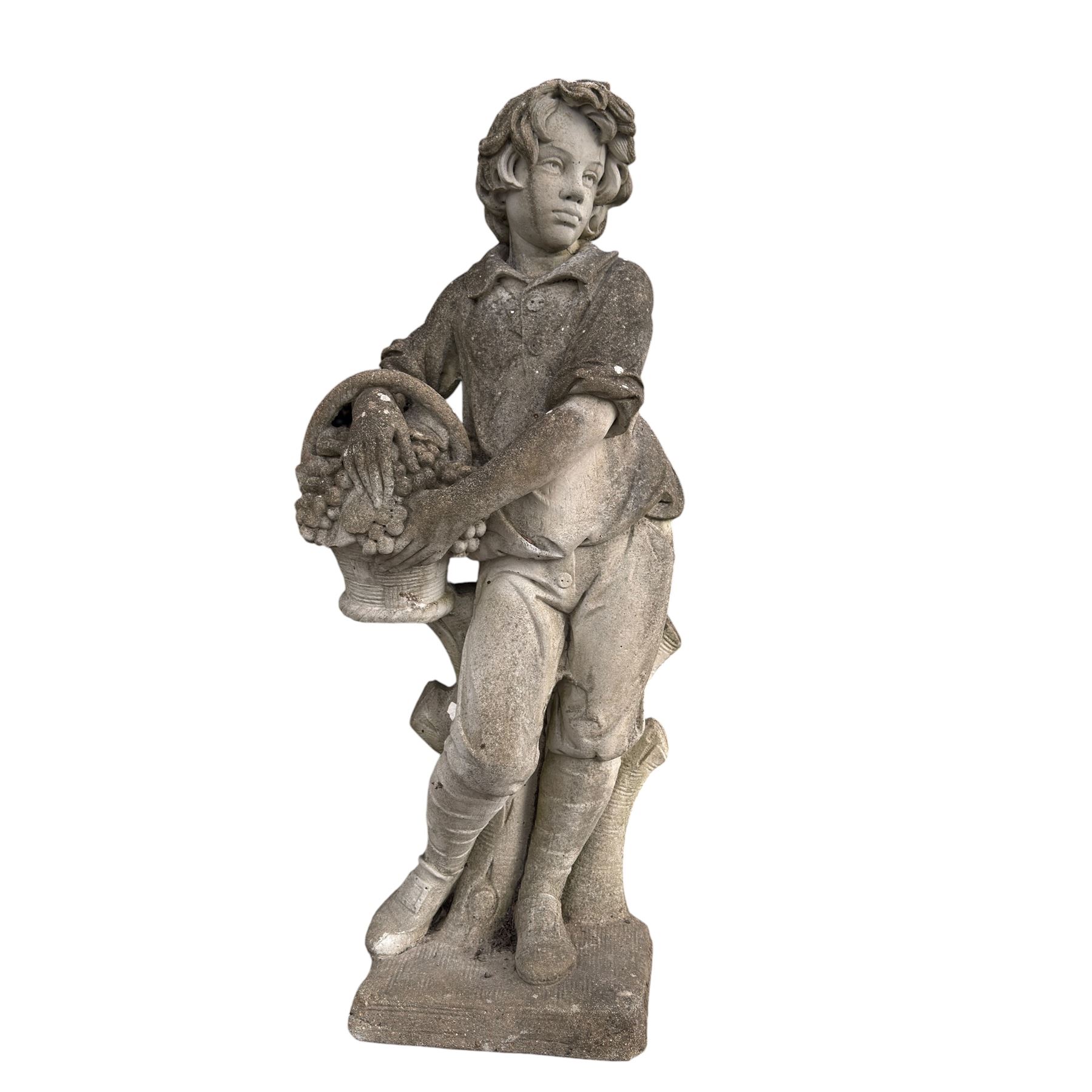 Haddonstone - weathered cast stone garden statue of a boy holding a basket of grapes, modelled with curled locks of hair wearing a tunic and breeches leaning against a naturalistic tree stump, on square base