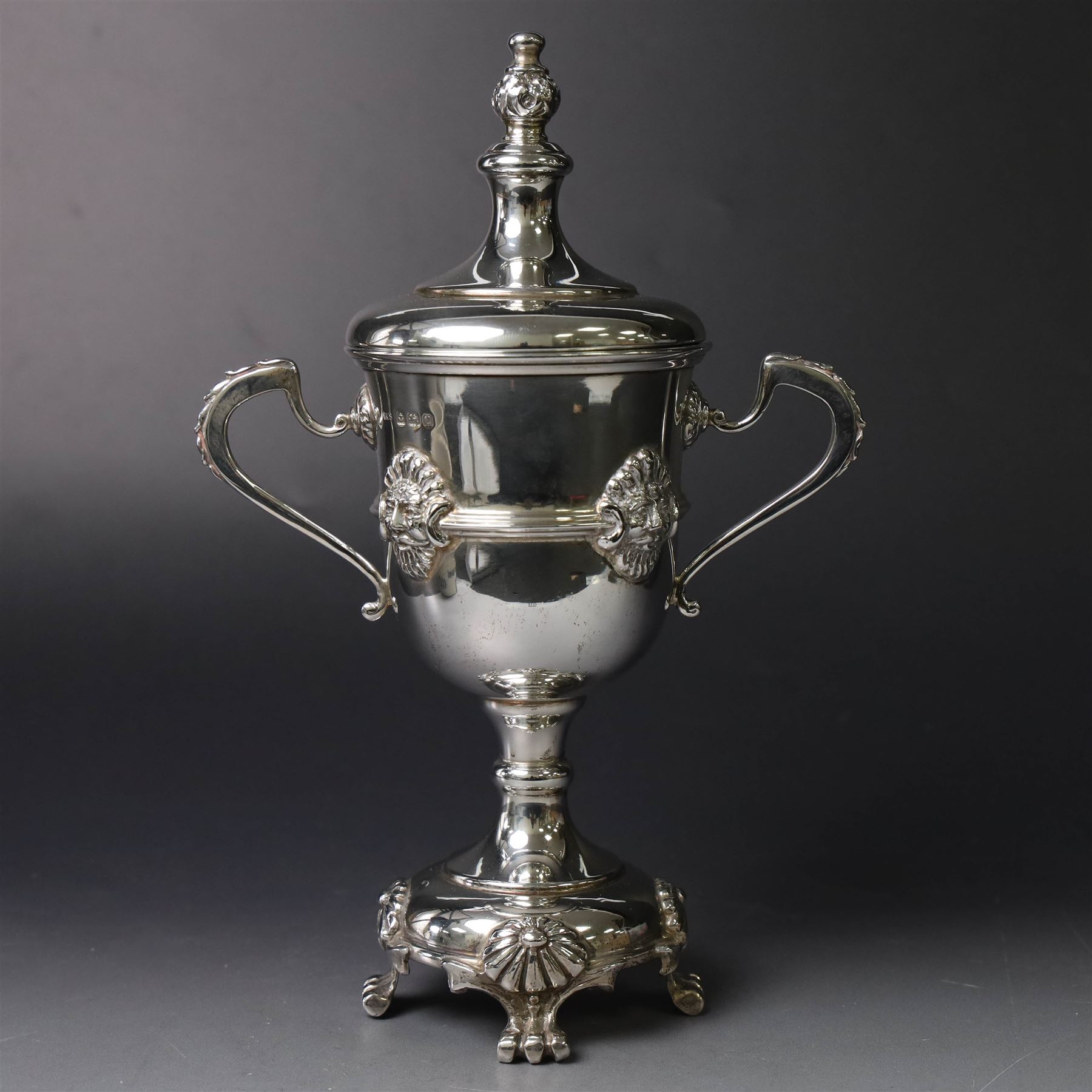 Mid 20th century silver twin handled trophy cup and cover, the bowl with central mask mounted girdle upon a knopped stem and spreading circular foot with flower head mounted paw feet, the tapering stepped cover with leaf moulded knop finial, hallmarked Vaughton & Sons, Birmingham 1938