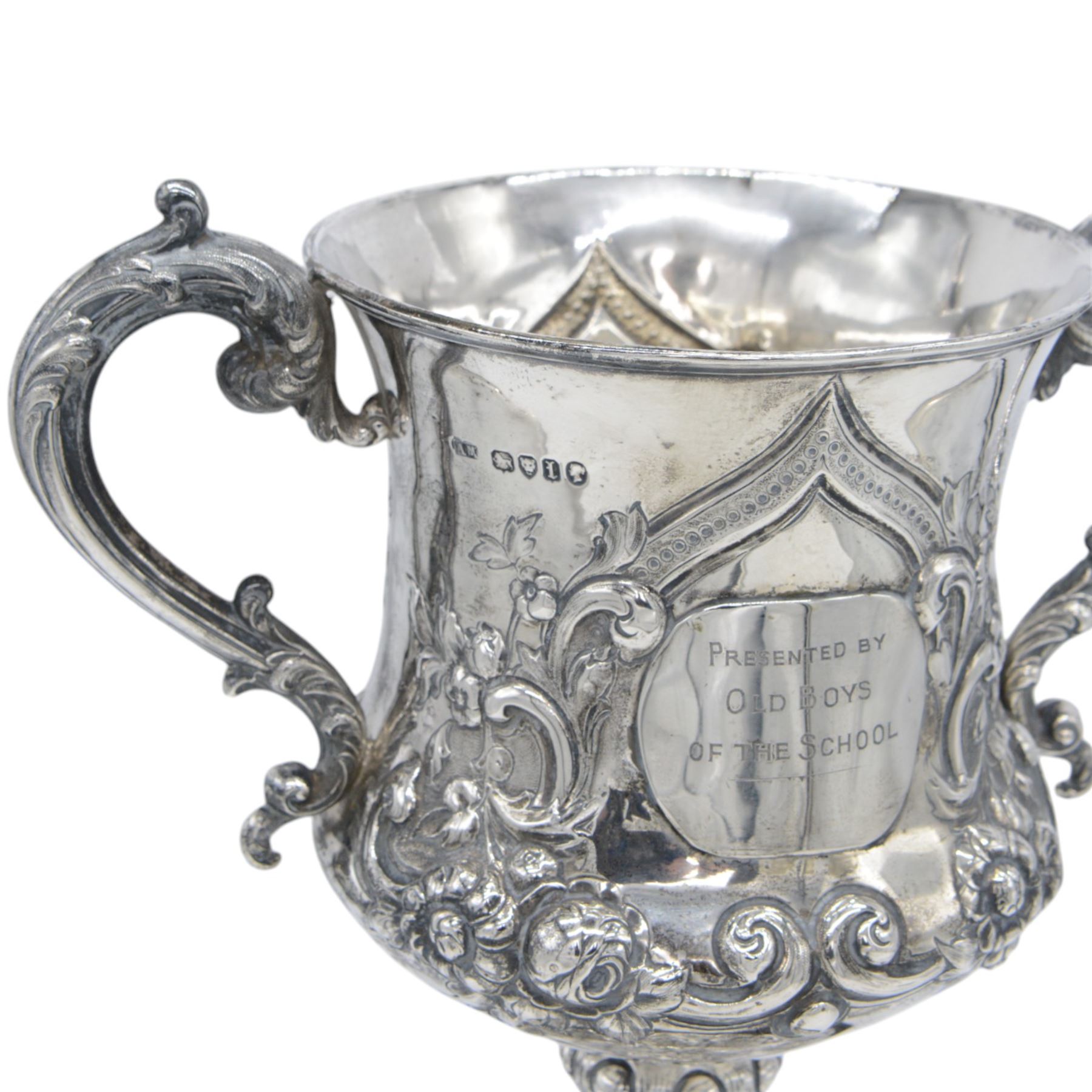 Victorian silver twin handled trophy, the bowl embossed with floral and scrolling decoration, with presentation engraving to body and twin acanthus capped C scroll handles, upon a lobed foot, hallmarked London 1866, maker's mark AM probably for Alexander Macrae, upon an ebonised wooden plinth, trophy only H25.5cm