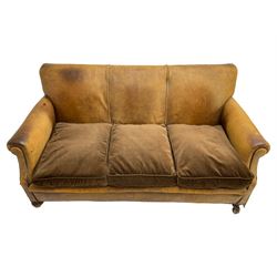 Early-to-mid-20th century three seat sofa, upholstered in worn tan leather with studwork, loose cushions upholstered in brown fabric, on compressed bun feet with castors