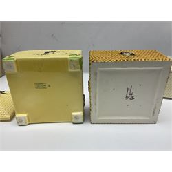 Four square honey boxes with lids,  each decorated with honeycomb pattern and finished with a bee finial