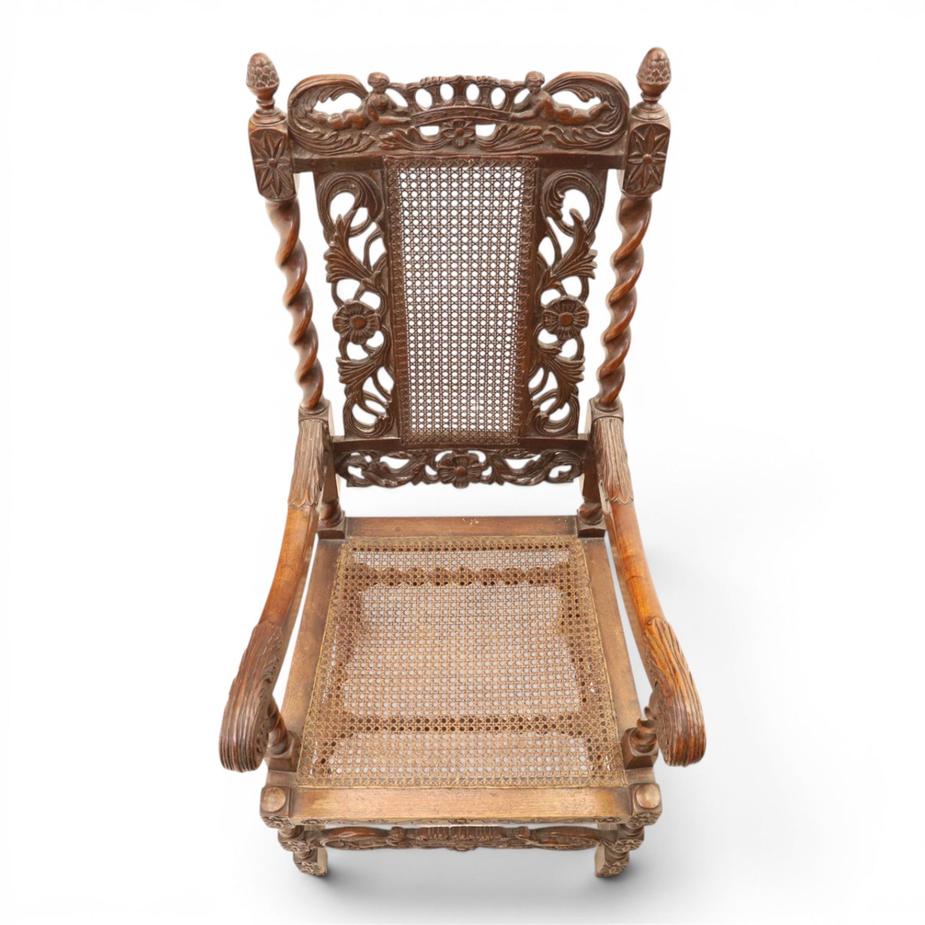 Late Victorian Jacobean Revival oak armchair, the caned back within a pierced and carved foliate frame surmounted by acorn finials, carved scroll arm supports, caned seat, on barley twist supports united by stretchers and carved front rail