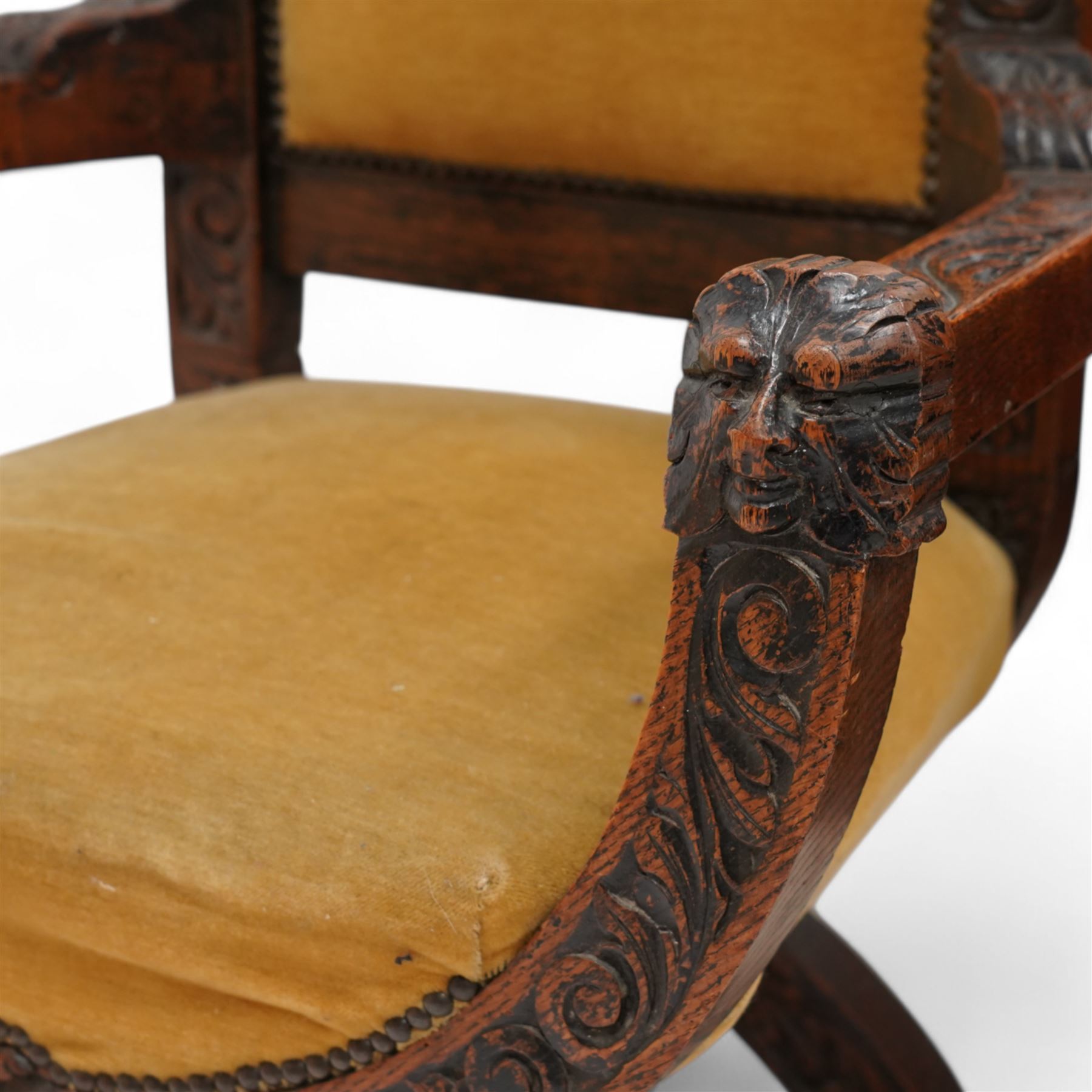 Victorian heavily carved oak X-framed throne chair, the cresting rail carved with mask and curling foliage, upholstered in mustard fabric, the arms and frame carved with scrolling foliage, united by turned stretchers 