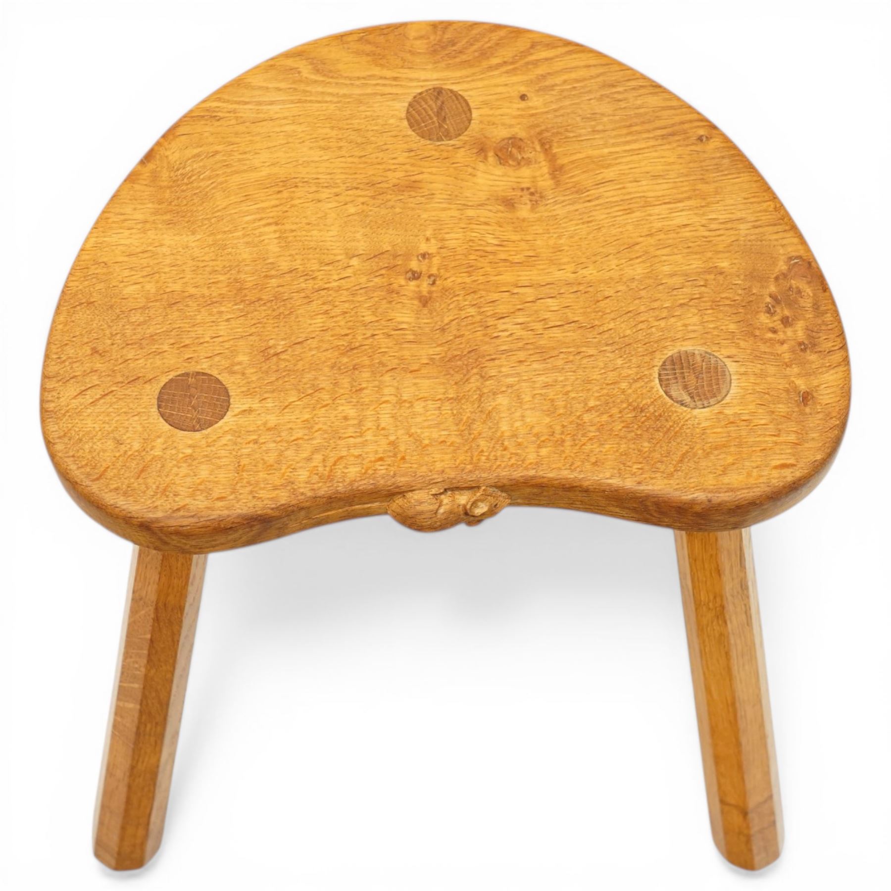 Mouseman - oak three-legged stool, dished kidney-shaped seat with burr inclusions, raised on three octagonal splayed supports, with carved mouse signature, by the workshop of Robert Thompson of Kilburn