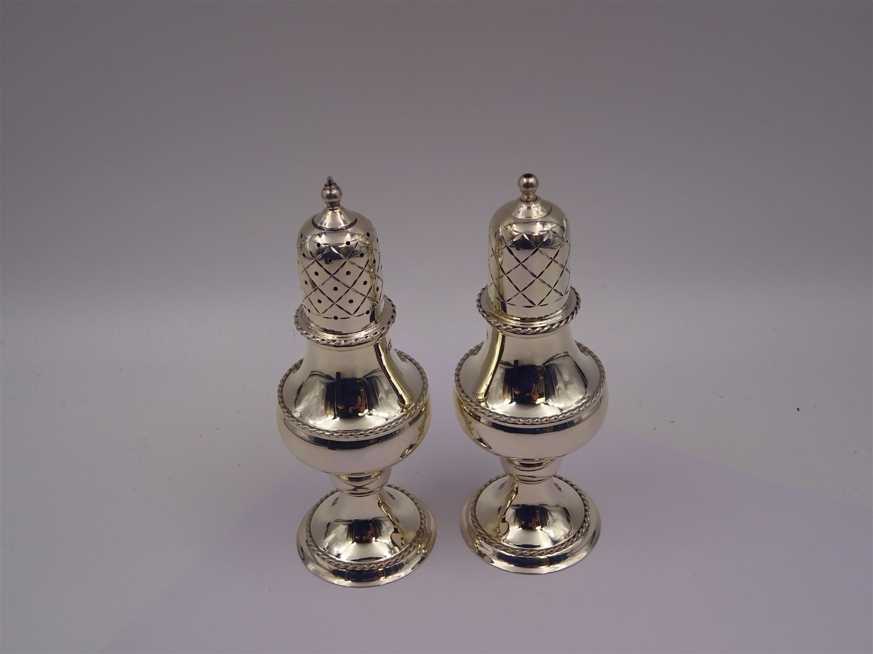 Modern silver two piece cruet set, comprising salt shaker and pepper shaker, both of waisted form with engraved rope twist borders, the removable pierced covers each with engraved lattice decoration, upon a circular spreading foot, hallmarked Laurence R Watson & Co, Birmingham 1989, H14.5cm, contained within velvet lined fitted case