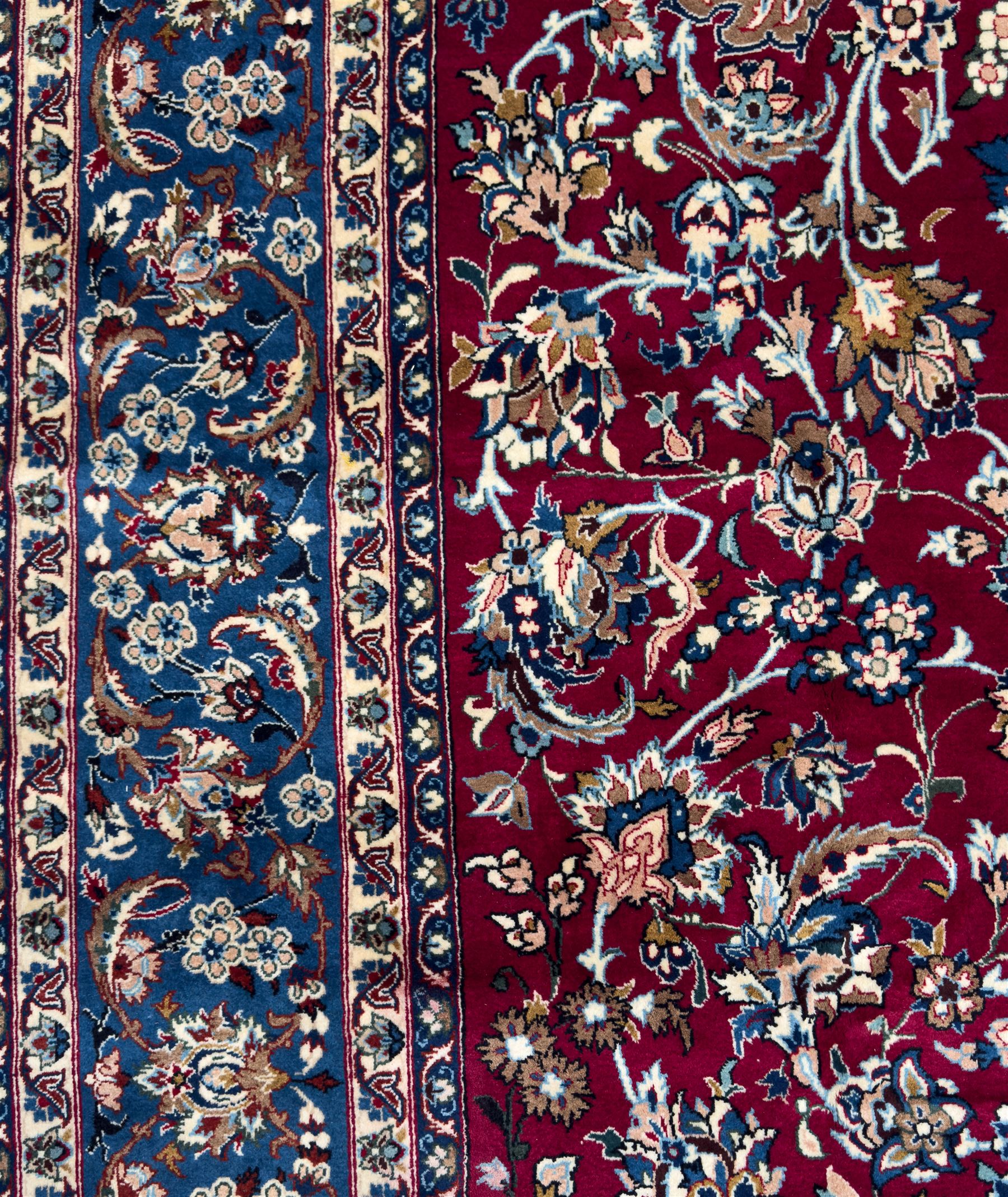 Central Persian Yazd hand-knotted rug, madder red field with scrolling vines, palmettes, and rosettes around a cusped lozenge medallion within a blue ground border of palmettes and flowerheads, 366cm x 250cm