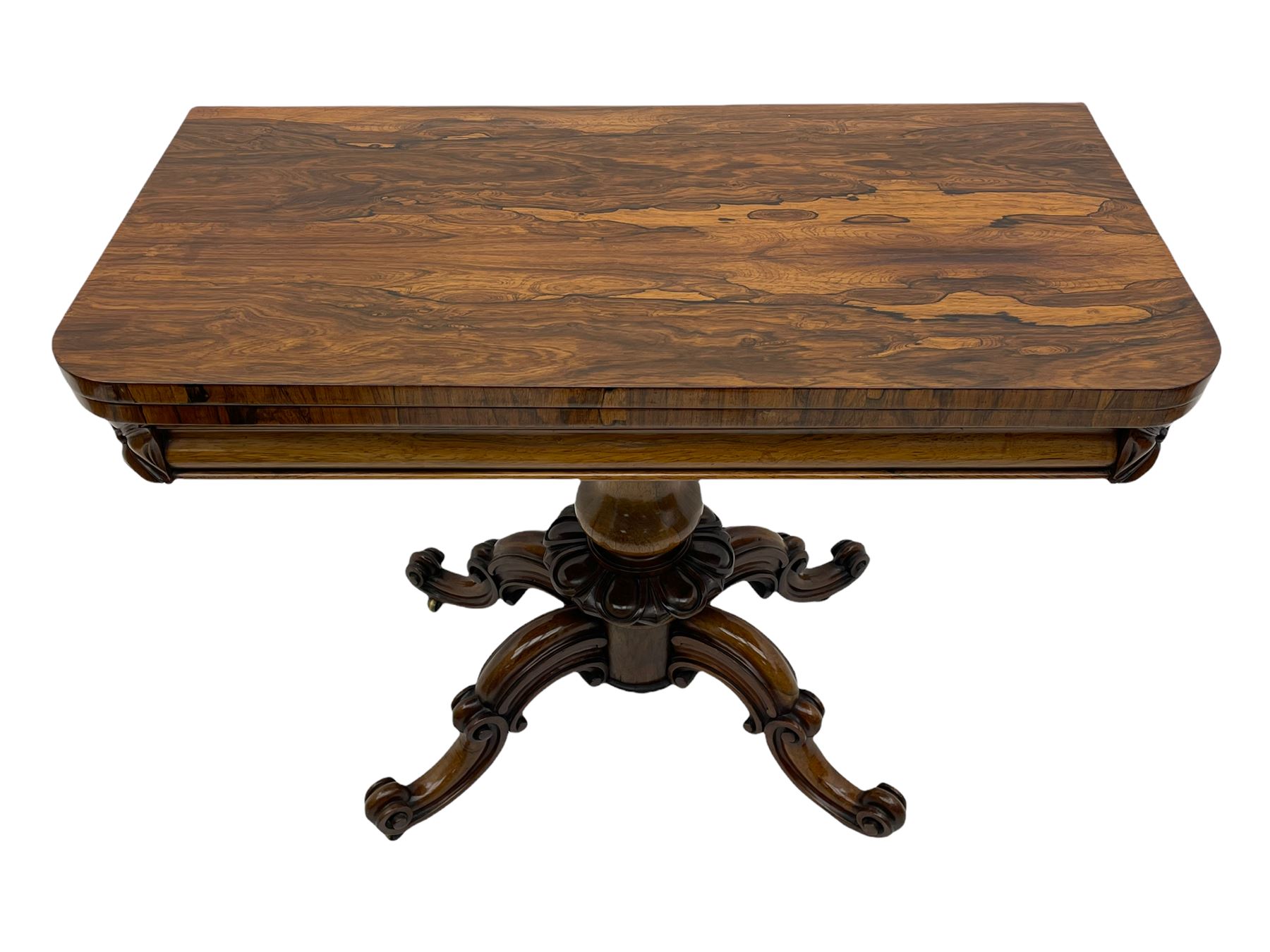 Victorian figured rosewood card table, fold-over swivel top with circular baize lining, moulded frieze with stylised flower head carving to corners, turned column with egg and dart decoration, on quadruple splayed c-scroll carved supports, with brass castors