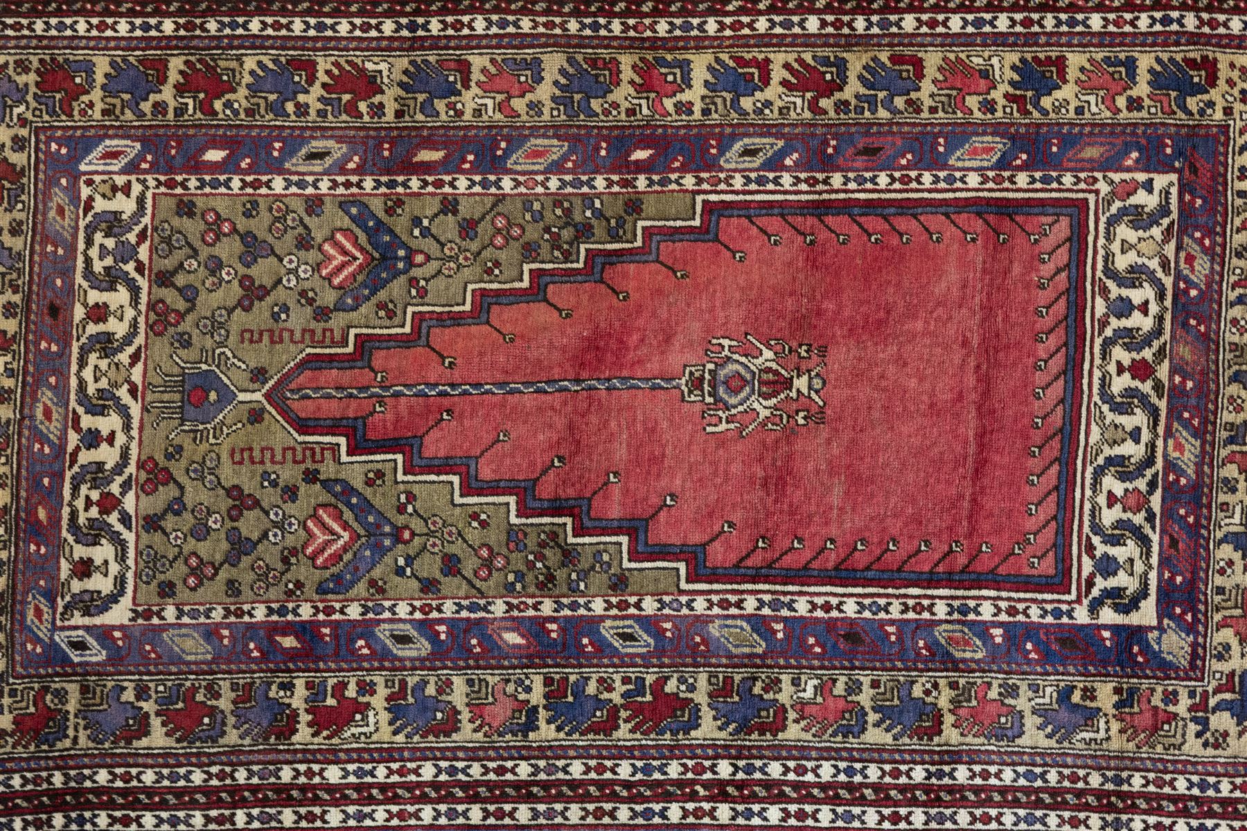 Persian Qashqai prayer rug, traditional tribal palette of red, indigo blue ivory and ochre, central field with stepped mihrab design in red, cantered by a stylized hanging lamp framed by a moss green spandrels, framed by boteh and floral motifs within multiple borders including an ivory border decorated with stylized animals in alternating colours 