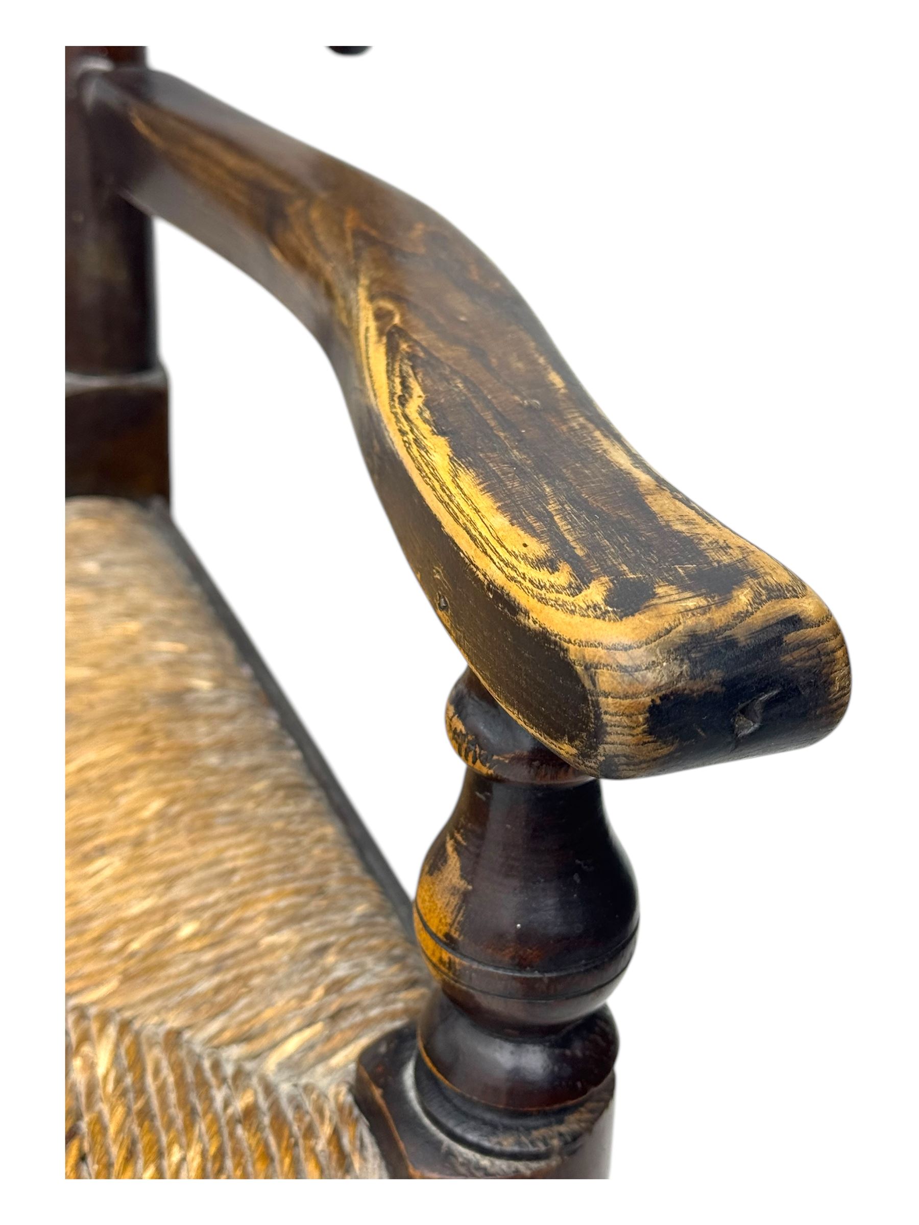 Early 19th century ash armchair, the back with winged spindles extending from a shaped top rail, above a splat of two rows of vertical spindles, with curved arms and a rush seat, raised on turned supports united by double stretchers terminating in castors