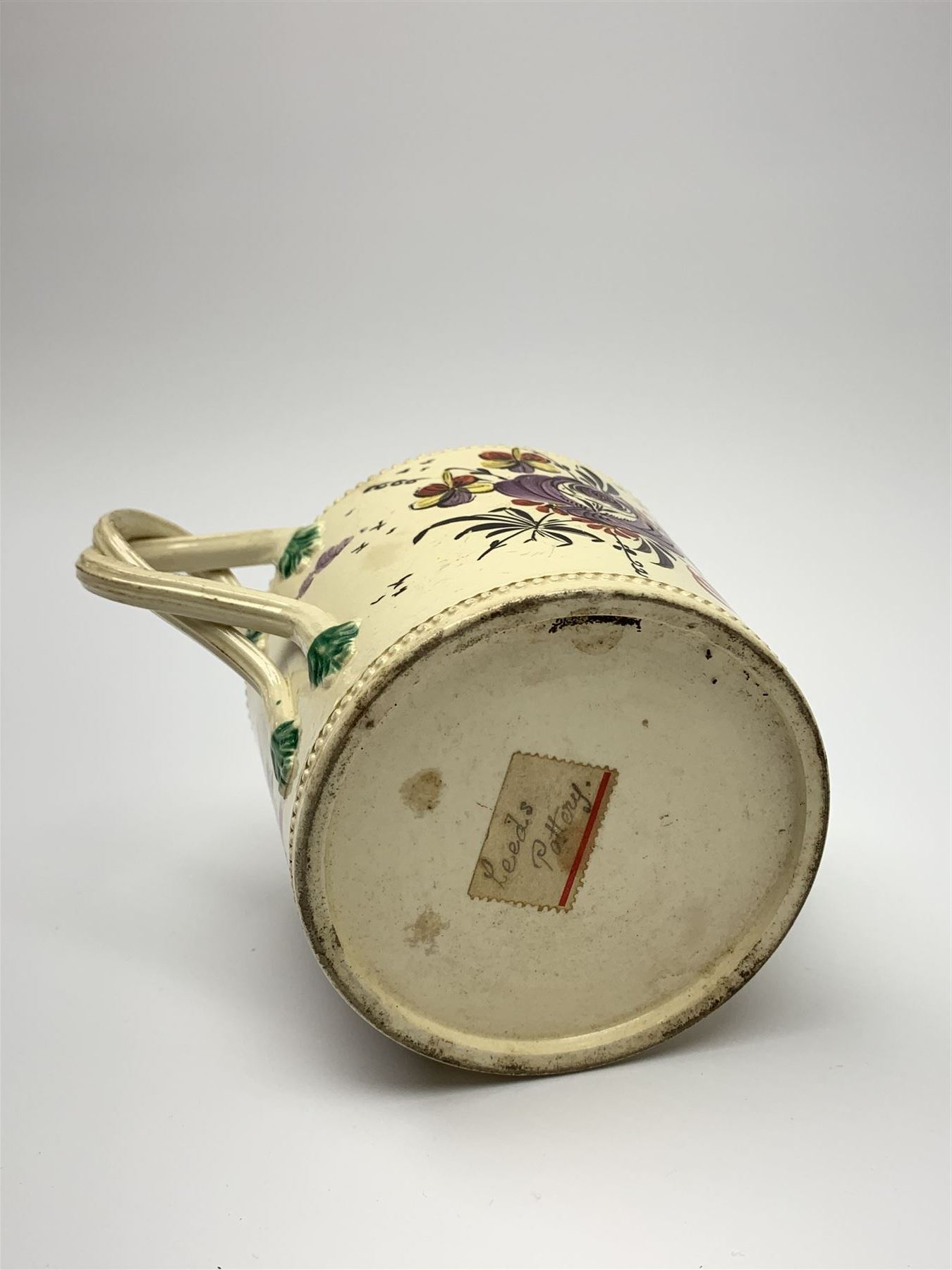 18th century creamware teapot, probably Leeds, with reeded entwined handle and floral finial to the cover, the body with hand painted polychrome decoration of figure to one side, and floral spray to the other, collectors paper label beneath inscribed Leeds Pottery, H11.5cm
