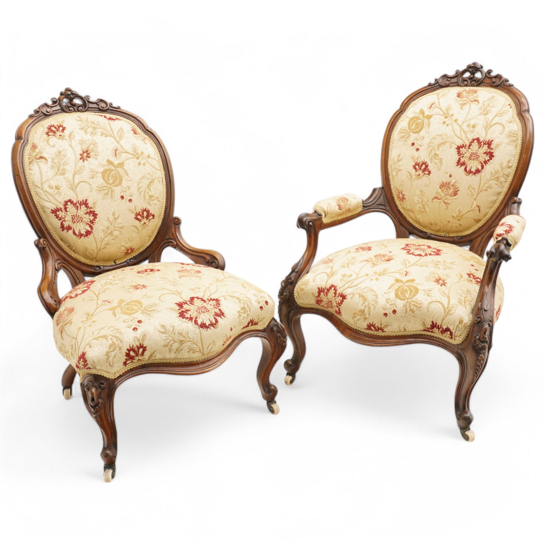 Victorian Ladies and Gentleman's carved walnut drawing room chairs, each with shaped cresting rail carved with scrolls and flowerheads, upholstered in pale gold floral fabric, raised on foliate-carved cabriole supports terminating to brass and ceramic castors