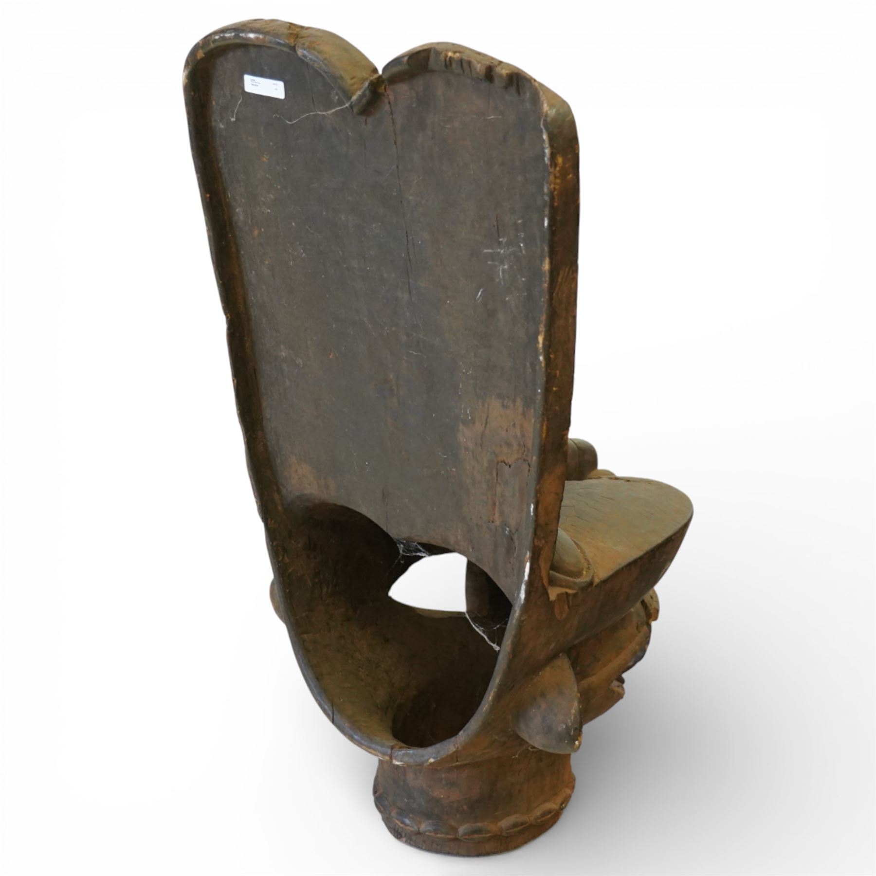 African carved hardwood ceremonial seat, monoxylous construction with twin dished seat wells, the tall back incised with repeating geometric triangular motifs, the front carved in the form of a tribal mask with projecting features, raised on a cylindrical base with ribbed and textured carving