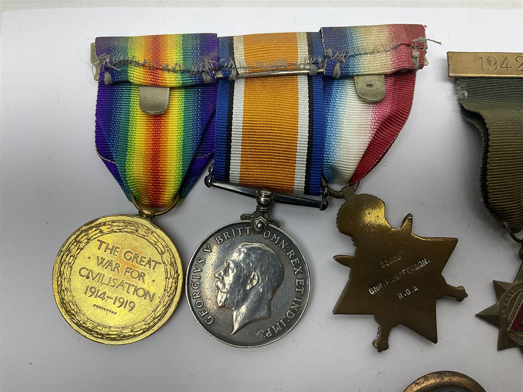 Made-up group of three WWI medals comprising 1914 Star awarded to 23598 Gnr. F. Jefferson R.G.A., British War Medal and Victory Medal with names removed; with ribbons on wearing bar; 1942 Motorist's Medal and small quantity of cap badges, Royalty badges etc