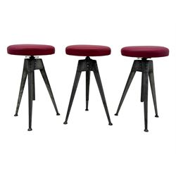 Contemporary industrial design riveted metal table, by repute fashioned from salvaged aeroplane parts, with a circular glass top on a tripod base, accompanied by three adjustable stools upholstered in burgundy