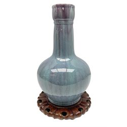 Blue glazed vase of squat baluster form with elongated neck, with merging streaked purple and light blue decoration, raised upon carved circular hardwood stand, H34cm