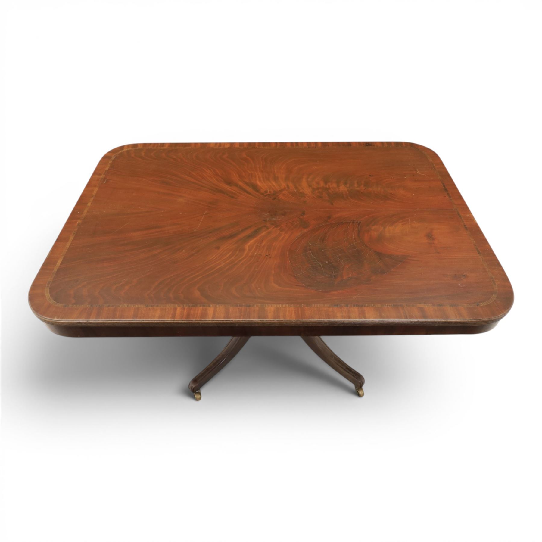 Regency mahogany tilt-top dining table, crossbanded rounded rectangular top, raised on a splayed base, terminating in brass castors