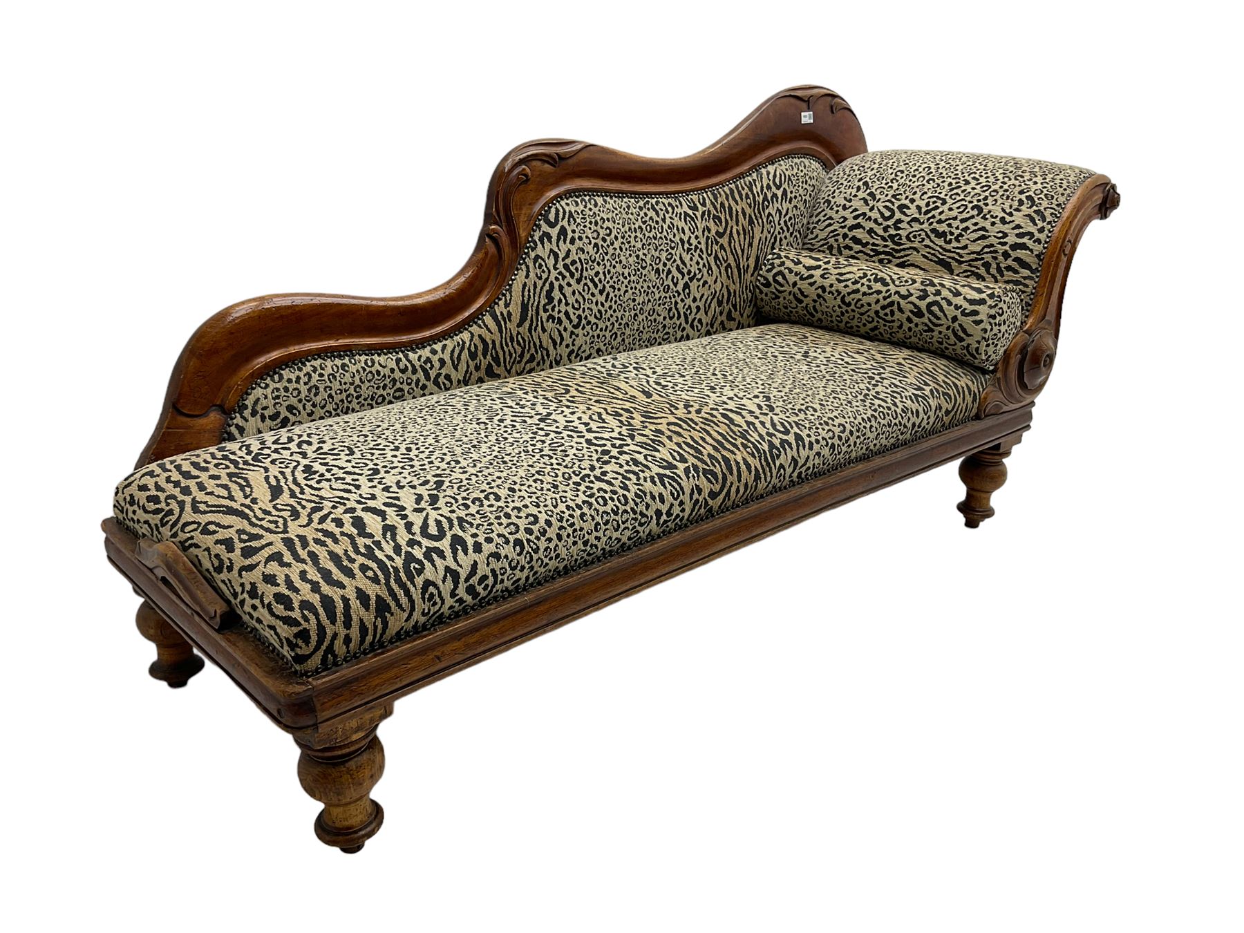 Victorian mahogany framed chaise longue, shaped arm carved with acanthus leaves, the scrolled back with applied carved rosettes,upholstered in monochrome leopard print fabric with bolster cushion, raised on turned supports