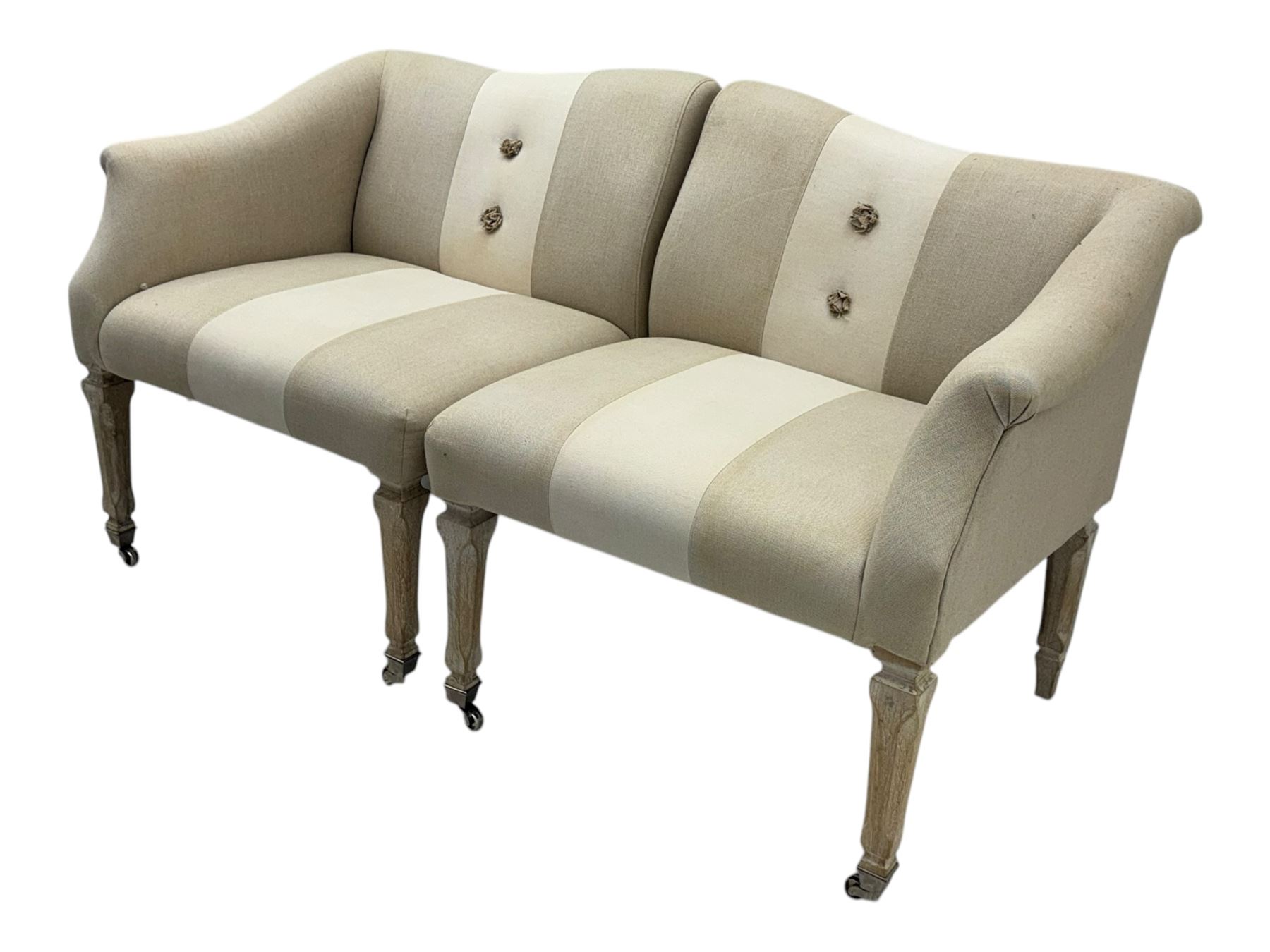 Pair of contemporary hardwood corner chairs, upholstered in broad alternating bands of neutral-toned fabric, each with two knotted rope buttons to the backrest, the whole raised on turned and lightly whitewashed supports terminating in castors