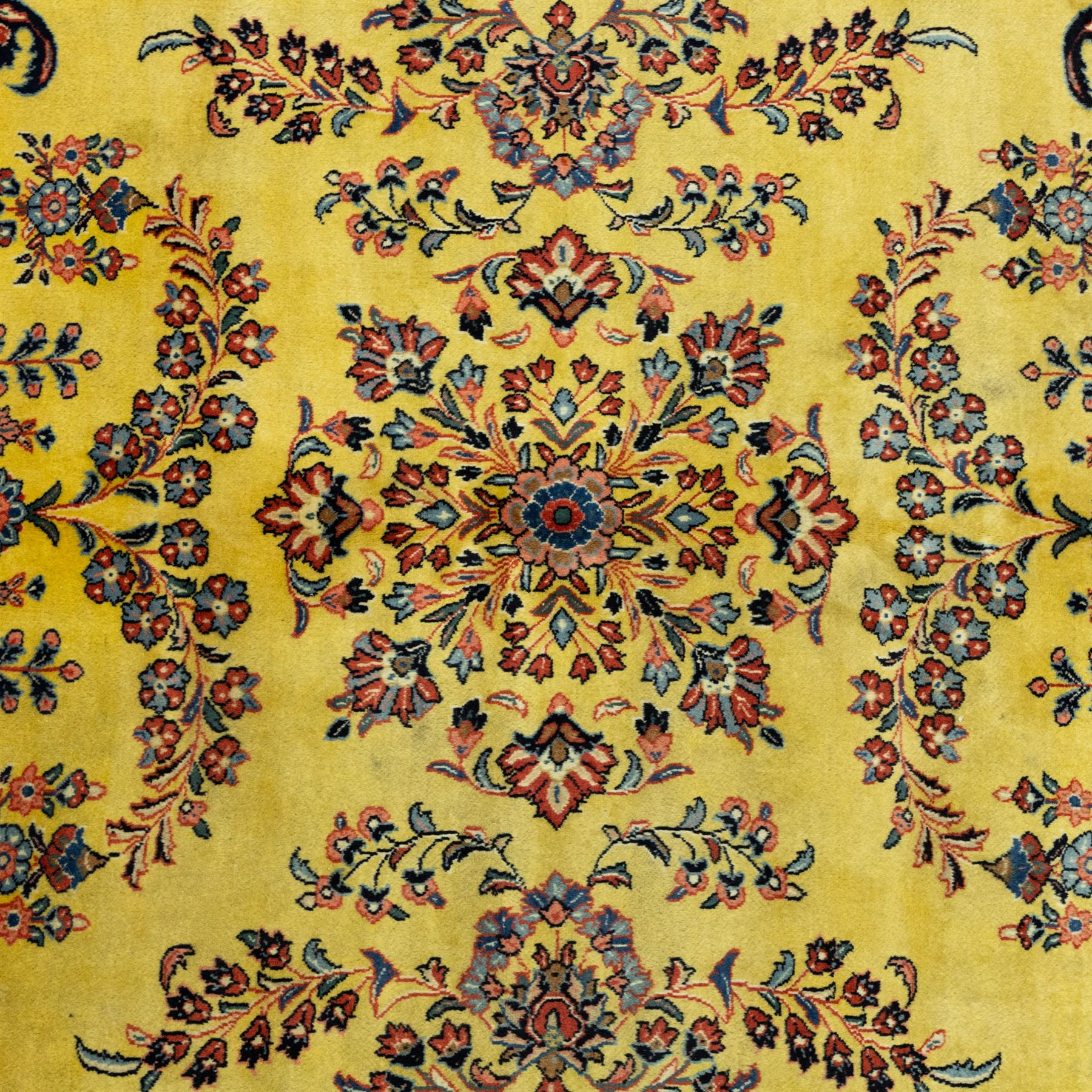 Persian Sarough hand-knotted carpet, golden yellow ground, with an all-over floral design centred by a small floral motif, the field decorated with mirrored flowering sprays, scrolling vines and dark navy foliate corner motifs, enclosed by a terracotta border with repeating flowerheads and palmettes, flanked by narrow guard stripes, with cotton fringes