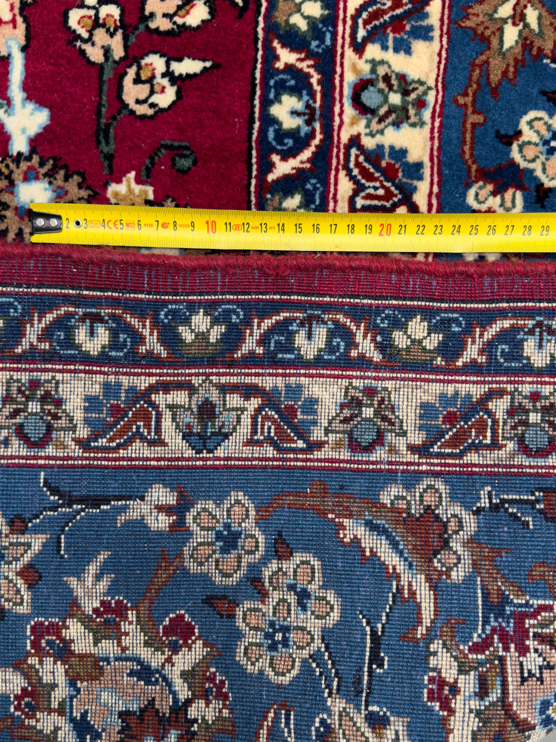 Central Persian Yazd hand-knotted rug, madder red field with scrolling vines, palmettes, and rosettes around a cusped lozenge medallion within a blue ground border of palmettes and flowerheads, 366cm x 250cm