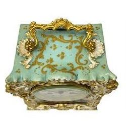 Continental - early 19th century porcelain mantle clock with a French eight-day movement, rectangular case with raised gilt rococo decoration and carrying handle, hand painted panel to the front portraying a picturesque lakeside scene and two figures in 18th century dress, contrasting light green background with raised gold decoration to the sides and a depiction of flying birds within a scrollwork cartouche, white enamel dial with a cast brass bezel, Roman numerals, minute track and steel trefoil hands, dial inscribed Henry Marc, count wheel striking movement with a silk suspension, striking the hours and half hours on a bell. 

