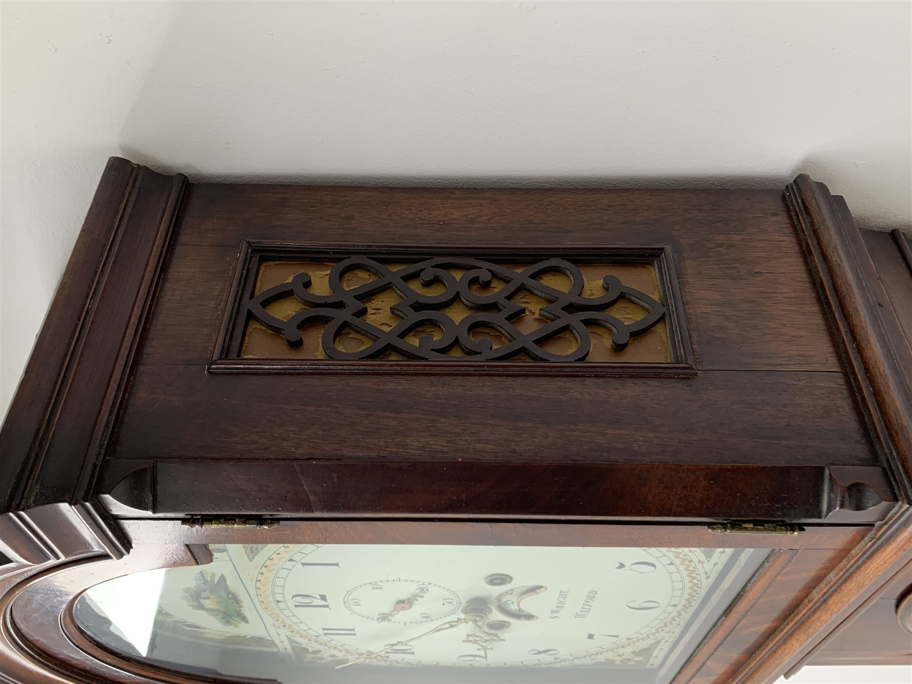 George III mahogany longcase clock, the hood with stepped moulded arch pediment above glazed door, fret work grille to each side, figured trunk door and base, enamel Arabic dial painted with country house scene and floral spandrels signed 'S. Wright, Watford', subsidiary seconds dial and date aperture, eight day movement striking the hours on bell, H212cm (two weights and pendulum)