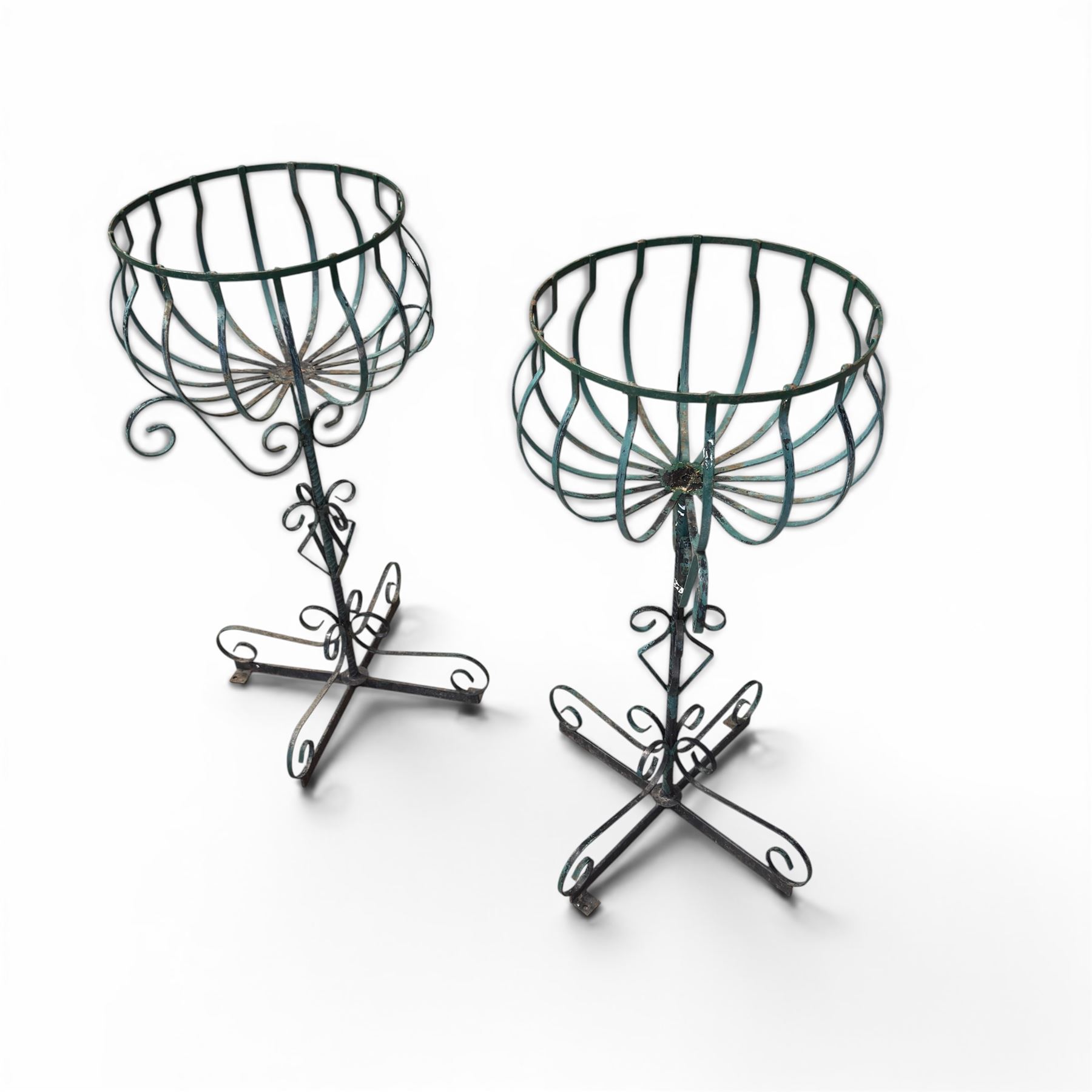 Matched pair of antique metal plant stands, each with circular strapwork basket tops, the scrollwork supports raised on an X-form base, in green painted finish with rustic patina