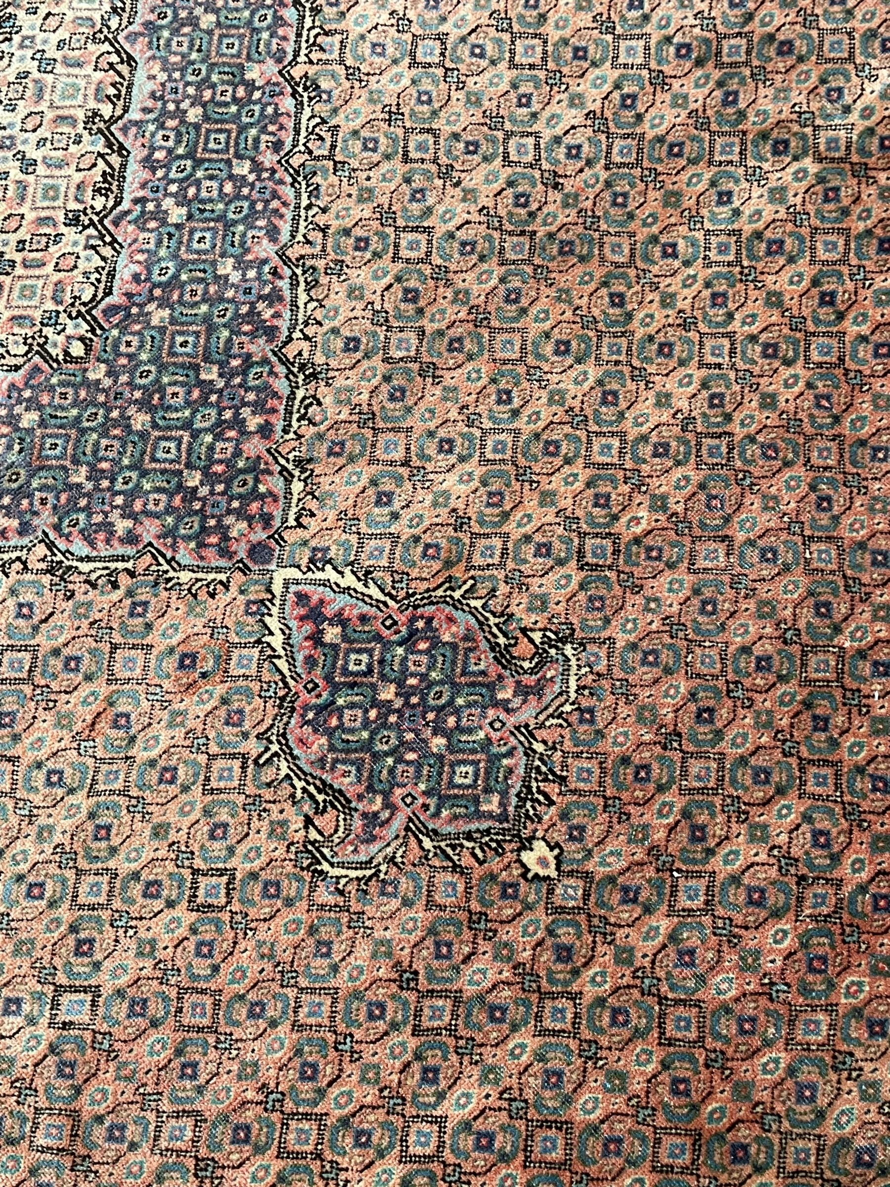 Persian Bidjar peach ground carpet, central pole medallion enclosed within lozenge field and spandrels, decorated all over with small Heratti motifs, the main border with trailing pattern decorated with stylised plant and Boteh motifs, within two triple band guard stripes with repeating flower head decoration 
