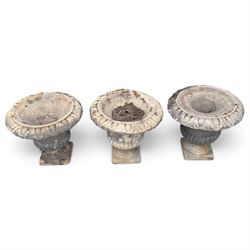 Set of three 19th century weathered carved sandstone garden urns of Neoclassical campana form, the broad everted rim carved with pointed egg-and-dart motifs, above a plain waisted bowl with gadrooned underbelly, on moulded rope-twist socle and square plinth base