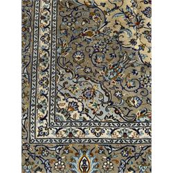 Central Persian Kashan pale khaki and ivory ground carpet, shaped central medallion enclosing small stylised motifs, the field decorated profusely with trailing foliate branches and plant motifs, guarded border with repeating floral design