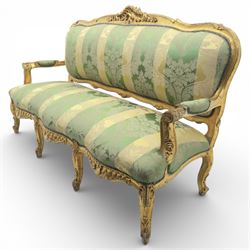 20th century French Louis XV style giltwood salon sofa, with shaped and moulded serpentine cresting rail carved with central scroll motif, padded back and seat upholstered in green and gold striped damask fabric, scroll carved open arms with padded rests, shaped apron carved with rocaille and foliate motifs, raised upon cabriole legs