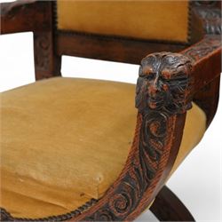 Victorian heavily carved oak X-framed throne chair, the cresting rail carved with mask and curling foliage, upholstered in mustard fabric, the arms and frame carved with scrolling foliage, united by turned stretchers 