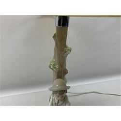Nao table lamp modelled as a boy playing the flute upon logs with two recumbent sheep at his feet, the stem modelled as a tree trunk, with fabric shade, with printed mark beneath, H46cm