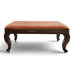 Victorian carved mahogany fender stool of generous proportions, the wide rectangular seat upholstered in rose fabric, shaped frieze rail over C-scroll and cartouche carved cabriole supports with scroll feet and brass castors