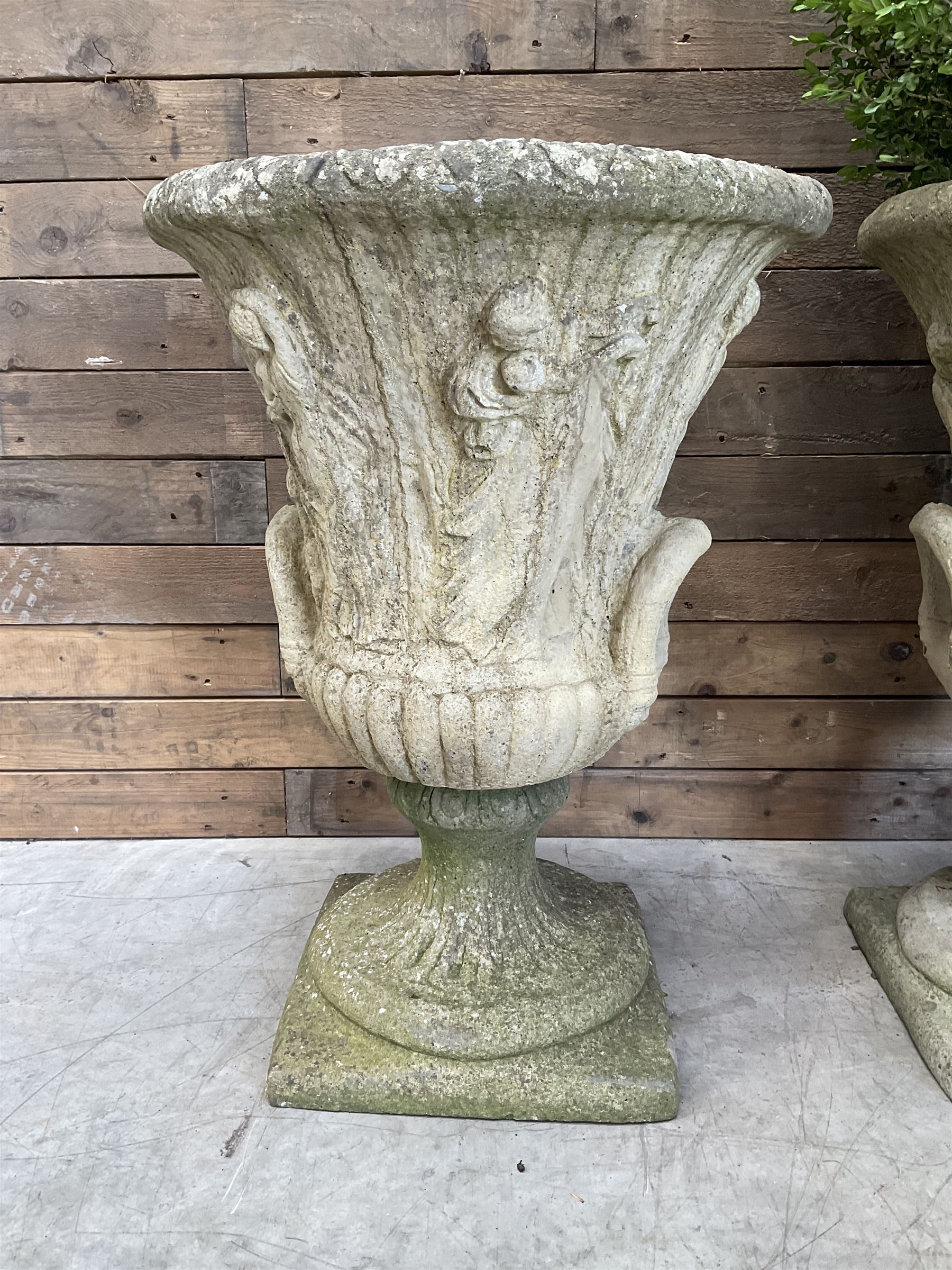 Set of four Victorian design cast stone Grecian urns, tapering form cast with figures and handles, square plinth bases