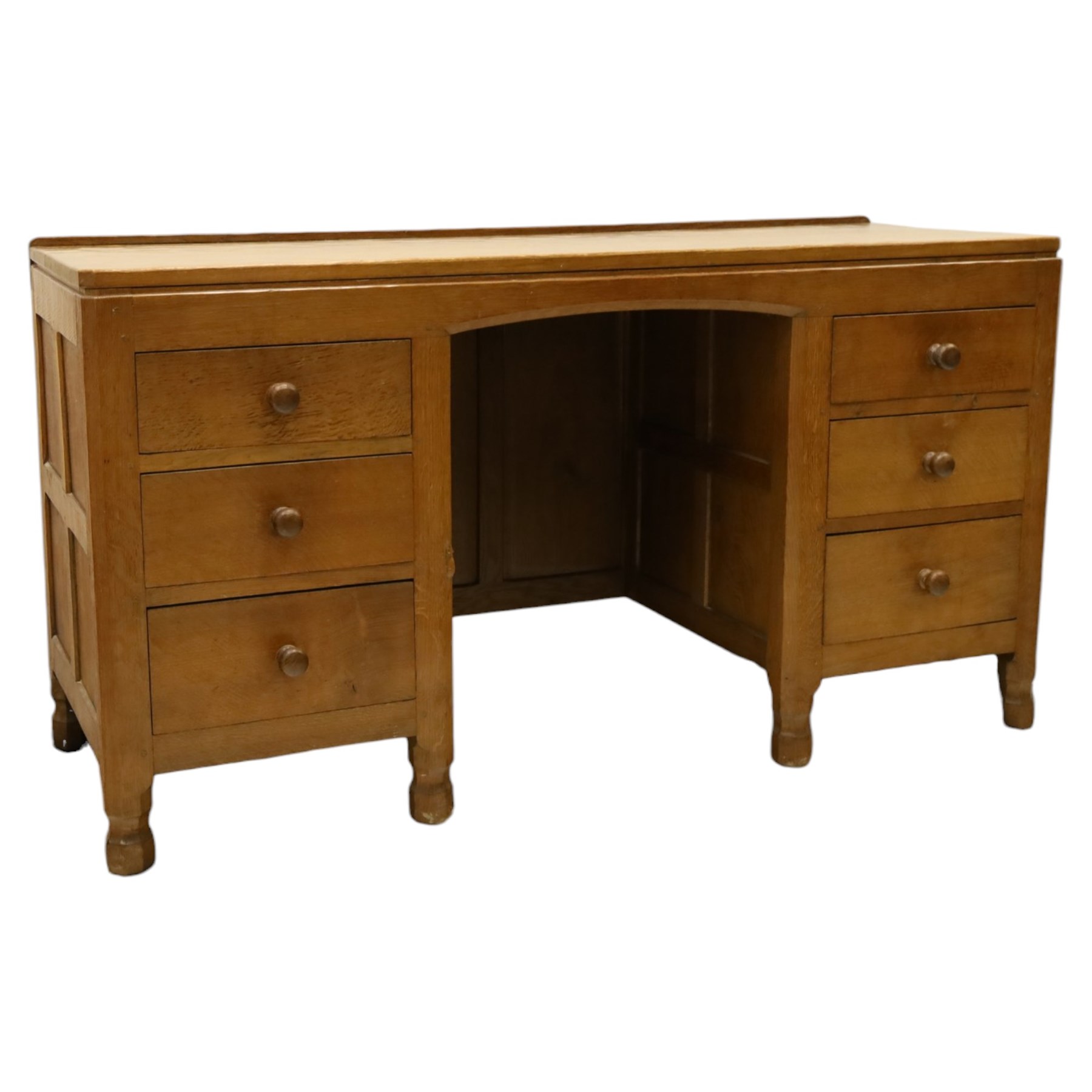 Mouseman - adzed oak kneehole dressing table or desk, the rectangular adzed top with raised back and canted corners, over an arched recessed kneehole flanked by three graduating drawers to each side with turned knob handles, raised on octagonal feet, with carved mouse signature, by the workshop of Robert Thompson of Kilburn