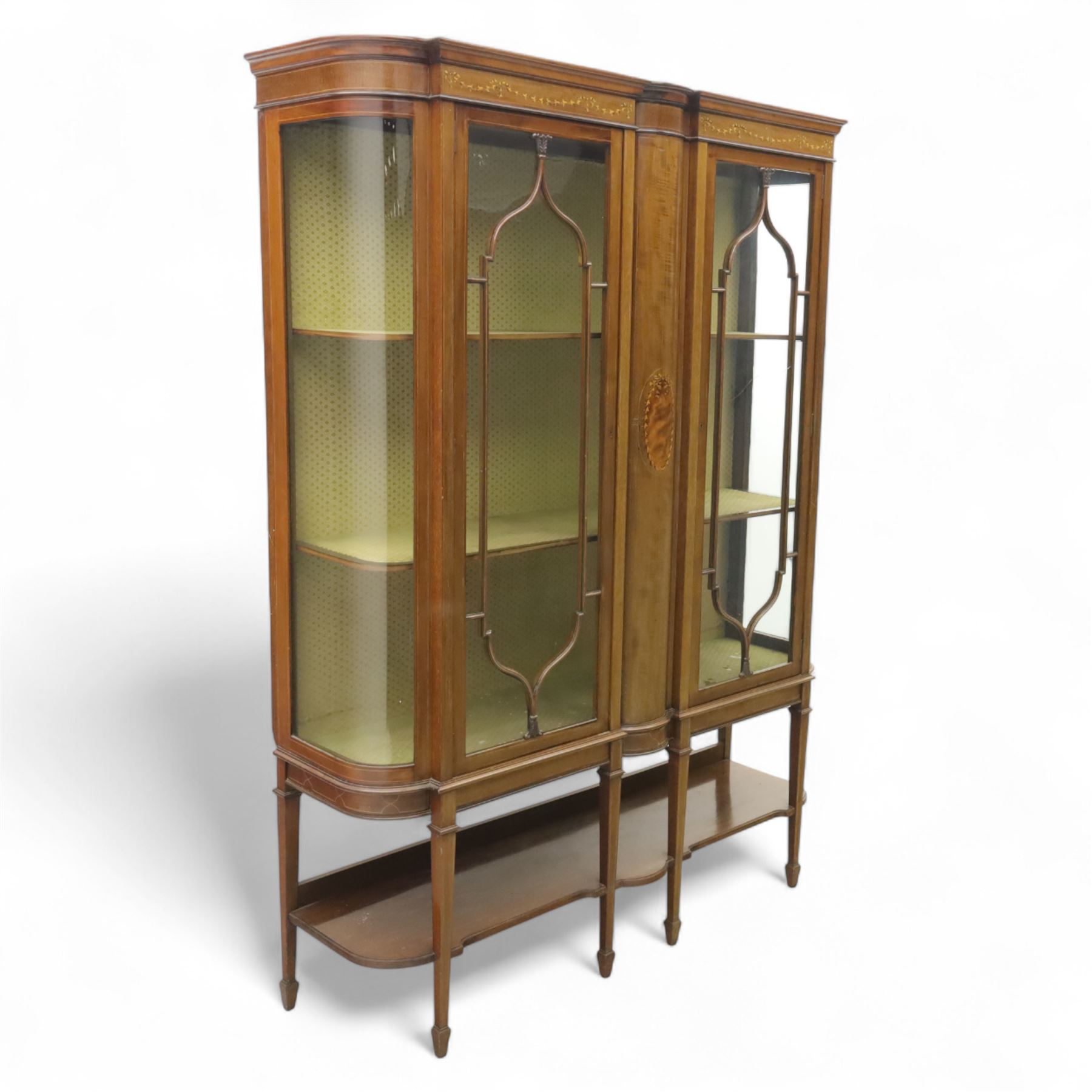Edwardian inlaid mahogany display cabinet, projecting moulded cornice over two glazed doors, flanked by curved glazed sides and central arched panel with floral medallion, raised on square tapering supports with spade feet united by undertier