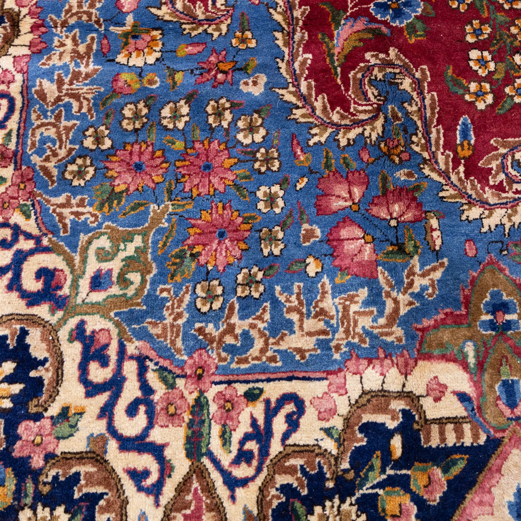 Large Central Persian Kirman hand-knotted carpet, raspberry red field, with central shaped medallion surrounded by an intricate arrangement of scrolling vines and floral sprays, within conforming spandrels and a pale blue border decorated with floral motifs, enclosed by guard stripes, with cotton fringe ends 