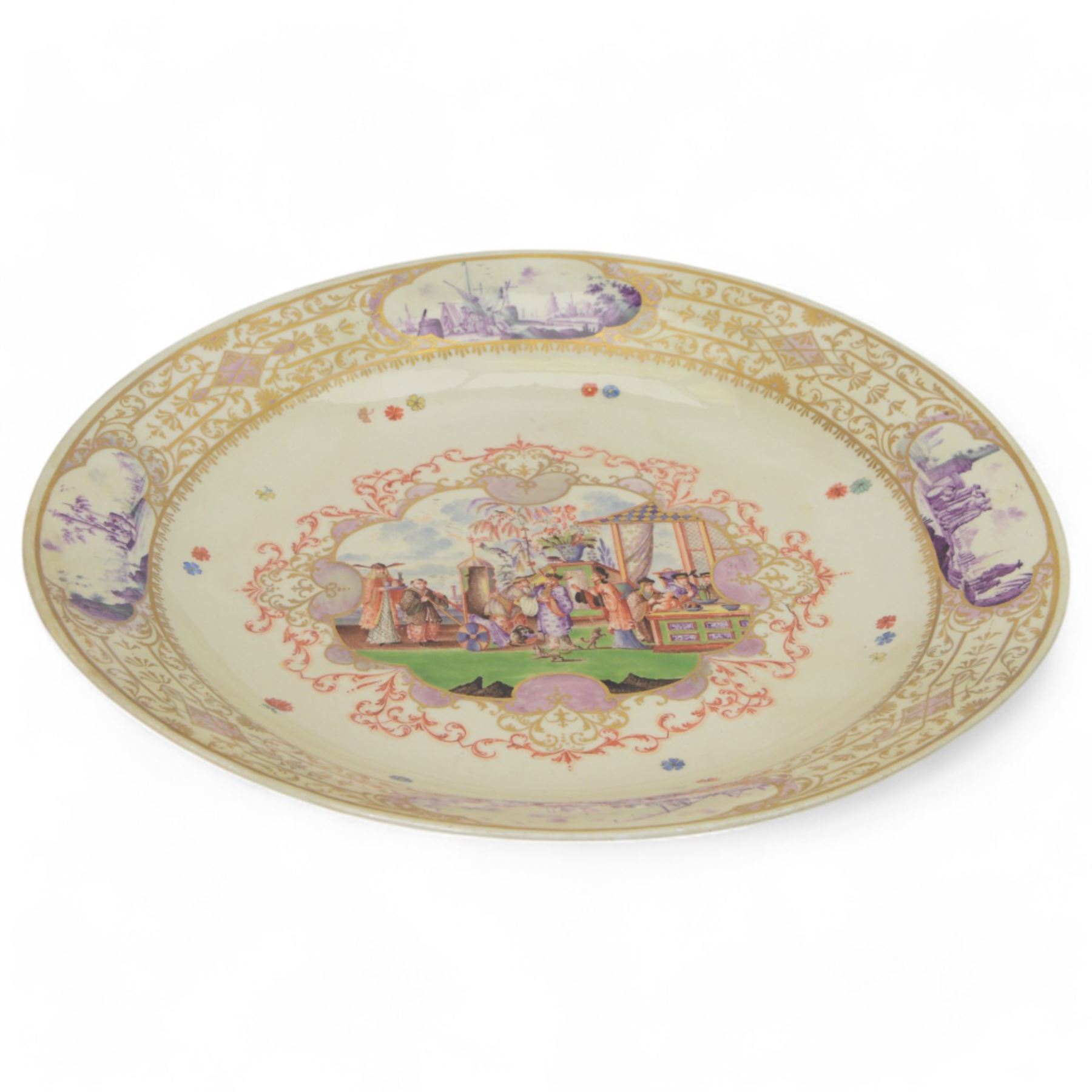 Large and impressive 18th century Meissen dish, finely painted with a chinoiserie scene to a central shaped reserve, depicting figures and attendants engaged in various pursuits, the reserve with gilt scrollwork edge, filled with Böttger lustre and detailed with iron red scrollwork, surrounded by flower heads, the rim with four quatrofoil Kauffahrtei scene panels of merchants and figures by a quayside in purple monochrome, with gilt scroll border, with under glazed blue crossed swords mark, and gilt gilders mark, D39cm

