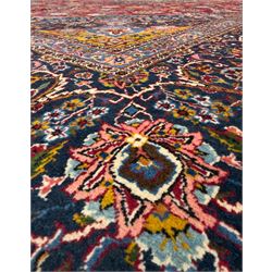 Central Persian Kashan hand-knotted carpet, madder red field with an intricate design of scrolling vines, palmettes, and rosettes with a central lobbed medallion with pendant motifs in shades of blue and ivory, and spandrels all within a blue-ground border of palmettes and flowerheads between multiple guard borders, 450cm x 335cm 