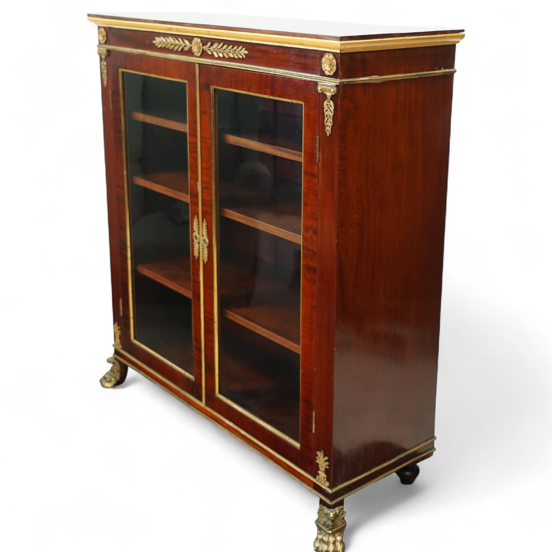 19th-century French Empire-style mahogany and gilt bronze-mounted glazed cabinet, rectangular top above frieze with applied gilt bronze laurel swags and rosettes with gilt brass borders, over two glazed panel doors enclosing three adjustable shelves, flanked by plain pilasters with applied mounts, raised on gilt bronze paw feet 