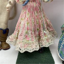Anna Meszaros Hungary - three hand made needlework figurines - young girl wearing a floral sun-dress and hat, standing on a grassy base holding a pink parasol H33cm; anthropomorphic cat wearing boots and a blue bow-tie H35cm; and young girl wearing a blue/green/white floral dress and lace bonnet, standing holding a floral posy H28cm (3)  Auctioneer's Note: Anna Meszaros came to England from her native Hungary in 1959 to marry an English businessman she met while demonstrating her art at the 1958 Brussels Exhibition. Shortly before she left for England she was awarded the title of Folk Artist Master by the Hungarian Government. Anna was a gifted painter of mainly portraits and sculptress before starting to make her figurines which are completely hand made and unique, each with a character and expression of its own. The hands, feet and face are sculptured by layering the material and pulling the features into place with needle and thread. She died in Hull in 1998.