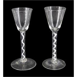 Two 18th century drinking glasses, the funnel bowls raised upon single series air twist, and single series opaque twist stems and conical feet, each approximately H16cm