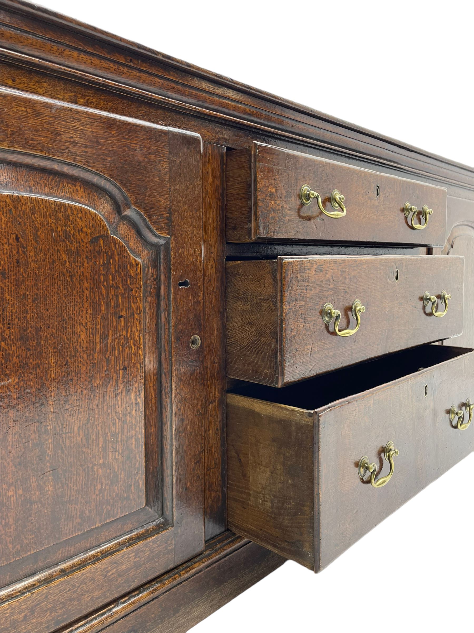 George III oak dresser base, rectangular top with rounded corners over moulded frieze rail, canted corners with turned quarter columns, fitted with three drawers with moulded edges flanked by two cupboards, enclosed by ogee arched fielded panelled doors, panelled sides, moulded plinth base