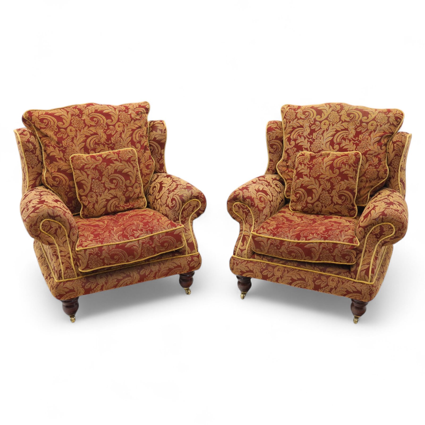 Duresta – pair of armchairs, upholstered in red and gold damask fabric with piped edges, scroll arms and loose feather-filled cushions, raised on turned wooden feet with brass castors